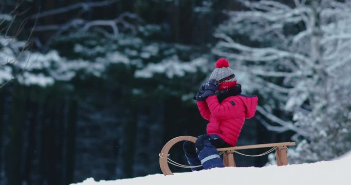 CU Cute little kid boy child preparing for a sledge ride down the hill. Child plays outdoors in snow, winter fun. 4K UHD 60 FPS SLOW MOTION 