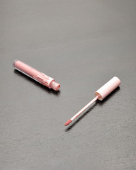 A lip gloss container and brush on a wooden background