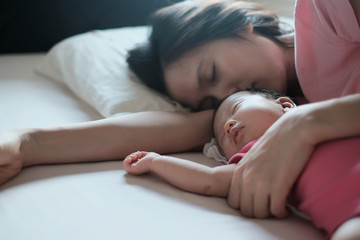 Close up beautiful portrait of beautiful young Asian mother hugging her newborn baby sleeping in bed in the morning. Focus on baby.Healthcare and medical love lifestyle of mother and baby concept.