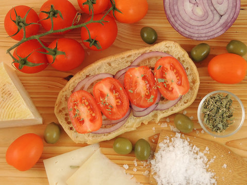 Friselle o Freselle su tavola di legno con pomodori ciliegia, cipolla rossa, olive e formaggio.