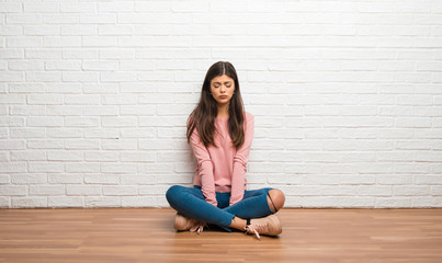 Teenager girl sitting on the floor in a room with sad and depressed expression