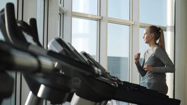 Attractive woman of middle age is running on tread mill in sport gym