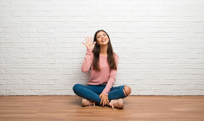 Teenager girl sitting on the floor in a room counting five with fingers