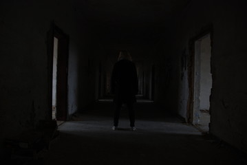 A woman from backside standing in dark corridor of abandoned decay building, urbex 