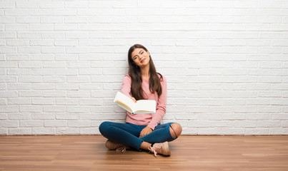 Teenager girl sitting on the floor in a room holding a book and giving it to someone