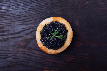 Black caviar in a tartlet against the dark wooden background © kcuxen