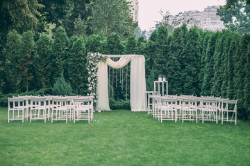 Beautiful wedding set up. Area of the wedding ceremony. Round arch, white chairs decorated with flowers, greenery. Cute, trendy rustic decor. Part of the festive decor, floral arrangement.