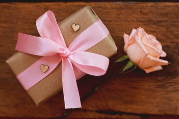 Lovely soft orange pink color rose tied by pink ribbon and brown gift box on wood table background, sweet valentine present concept