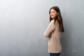 Teenager girl with sweater on a vintage wall keeping the arms crossed in lateral position while smiling