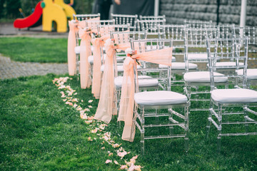 Fototapeta na wymiar Square wedding ceremony. Transparent chairs are decorated with flowers, greenery. Cute, trendy svdebany decor. Part of the festive decor, flower arrangement.