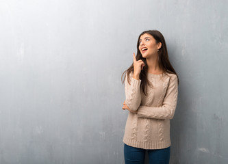 Teenager girl with sweater on a vintage wall pointing a great idea and looking up