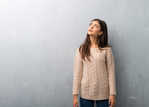 Teenager Girl With Sweater On A Vintage Wall Looking Up With Serious Face