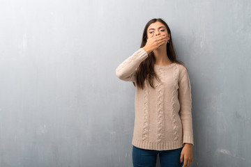 Teenager girl with sweater on a vintage wall covering mouth with hands for saying something inappropriate