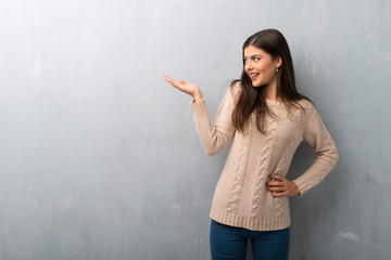 Teenager girl with sweater on a vintage wall holding copyspace imaginary on the palm to insert an ad