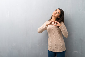 Teenager girl with sweater on a vintage wall making heart symbol by hands