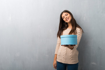 Teenager girl with sweater on a vintage wall holding a gift in hands