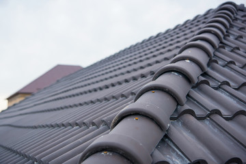 Building a house with a tiled roof. Directing wooden roof beams. Gray roof tiles and chimney of red brick. Unfinished house. Attic under the roof of the house. Round roof slope. © Yashkin Ilya