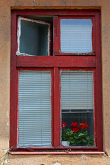 Fototapeta na wymiar Old, red painted window frame with a pane open, blinds drawn and red geraniums.