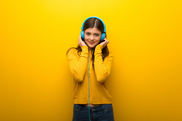 Teenager girl on vibrant yellow background listening to music with headphones