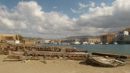 Fototapeta premium Old boat sprawling and gangway lying on the sand against the background of the promenade of Chania