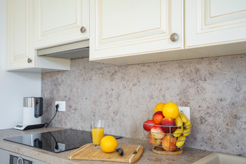 Kitchen interior. On the kitchen table next to the hob stands a vase with fresh fruits, and near it...
