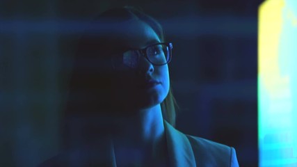 The woman in glasses walking in a dark room near a display. slow motion