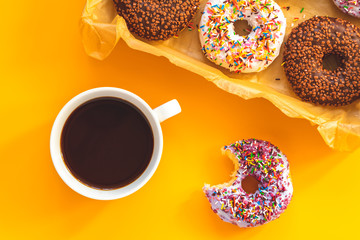Delicious glazed donuts in box and cup of coffee on yellow surface