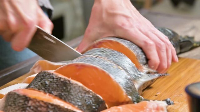 Close-up of female hands are cutting with a knife a large salmon on a wooden table of home cooking