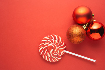 Creative concept photo of lolli pop popsicle candy and three christmas toys balls on red background.