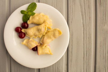 Dumplings with cherry in the white plate on the grey wooden  background.Top view.Copy space.