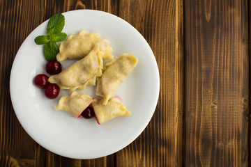 Dumplings with cherry in the white plate on the brown wooden  background.Top view.Copy space.