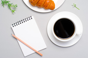 Freshly Baked Croissant, Cup of Coffee and Notepad on Grey Background