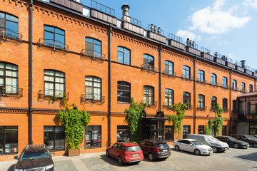 Huge red brick classic industrial building facade with multiple windows. Industrial background. Loft inspiration. Parked cars