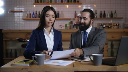 Cheerful female property owner signing terms of real estate contract with low rates after meeting real estate agent for house investment. Woman handshaking realtor after signing agreement at cafe.