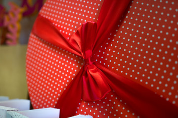 Close up of big red round box in polka dot with a ribbon and some postcards below. A red round gift-wrapped with a bow and postcards.