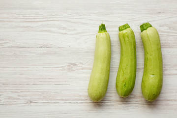 Fresh vegetable marrow zucchini on white wooden background, top view. Space for text.