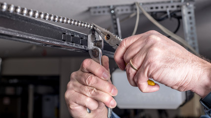 Man works with pliers to repair a garage door opener chain