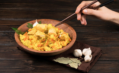 Pilaf with vegetables and chicken in a wooden bowl on a wooden background
