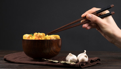 Pilaf with vegetables and chicken in a wooden bowl on a wooden background