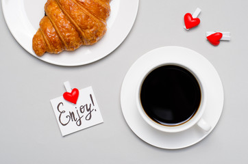 Freshly Baked Croissant, Cup of Coffee and Enjoy Note on Grey Background