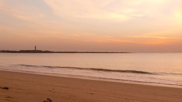 Sunset timelapse at Shivrajpur beach dwarka gujarat. Shows the very beauitful beach with its beautiful sand, waves lapping the shore, clouds and the lighthouse in the distance. Light changes from