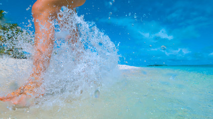 CLOSE UP: Unrecognizable woman splashes water as she runs along tropical beach.