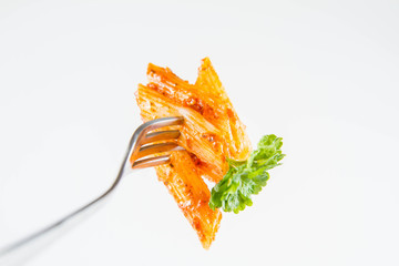 Penne with pesto decorated with parsley on a fork on a white background