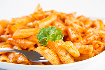 Penne with pesto decorated with parsley on a plate eaten with a fork on a white background