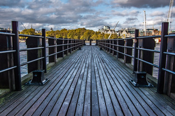 Obraz premium Landscape view of wooden platform on the river Thames.Trees and buildings in the background. London, United Kingdom.