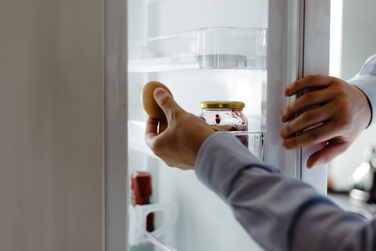 The Man Pulls Food Out Of The Fridge. View Of The Open Fridge. Using The Fridge, Cooling The Food To Extend The Shelf Life For Consumption. Taking Food Out Of The Fridge At Home, Preparing Meals.