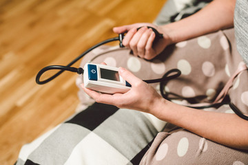 The topic of high blood pressure is hypertension disease. Close-up macro young caucasian woman hands using automatic tonometer to check pressure at home in bedroom on bed