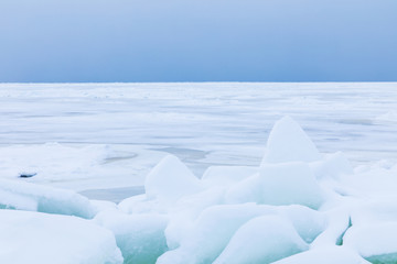 The winter gulf of the sea covered with snow and ice. White and blue beautiful landscape with cloudy sky, white surface of the sea and the heap of floes on the shore
