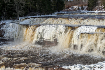 Lepreau Falls, New Brunswick, Canada, in winter. The falls are partially frozen, golden water flows over the rest.