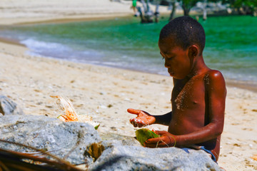 Poor malagasy boy breaking coconuts on the beach